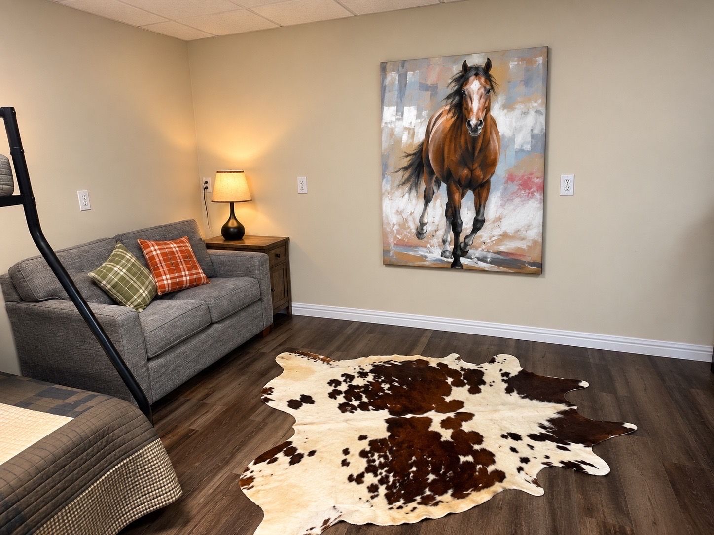 A room with a grey sofa, a lamp, a painting of a horse, and a cowhide rug.