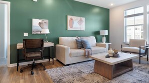 A modern living room with a green accent wall, a sofa, a coffee table, a desk, and a chair. - Landing | Amazing 2BD in Heath Brook (Ocala)