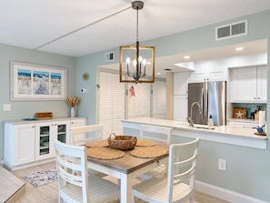 A modern kitchen with white cabinetry, a stainless steel refrigerator, and a dining area with a wooden table and white chairs. - La Coquina 2BR Beachfront - Gulf Views + Pool (Englewood)