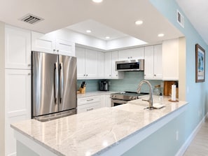 A modern kitchen with white cabinetry, stainless steel appliances, and a marble countertop. - La Coquina 2BR Beachfront - Gulf Views + Pool (Englewood)