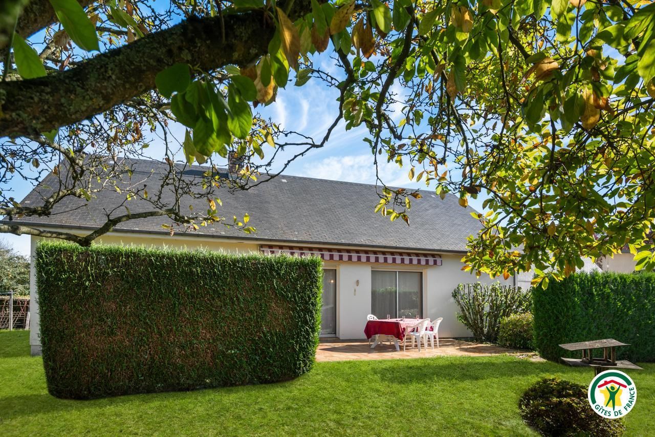 Une maison avec un jardin bien entretenu, une terrasse avec une table et des chaises, et un ciel dégagé.