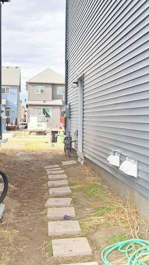 A narrow pathway leading to a building with a grey exterior. - Cozy Queen Suite|Private Basement (Calgary)