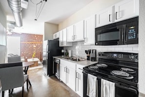 A modern kitchen with white cabinets, a black refrigerator, a microwave, and a stove. - Landing | Beautiful Studio, Gym (College Station)