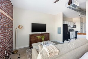A living room with a television, a sofa, a coffee table, and a brick wall. - Landing | Spectacular Studio, Gym (College Station)