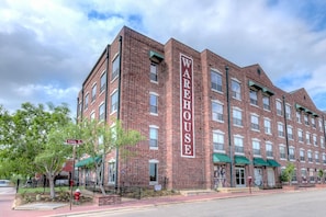 A multi-story brick building with a prominent 'WAREHOUSE' sign, a gated entrance, and a street view with a crosswalk and trees. - Landing | Spectacular Studio, Gym (College Station)