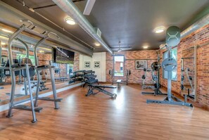 A gym with various exercise equipment, wooden flooring, and brick walls. - Landing | Beautiful 1BD, Gym (College Station)