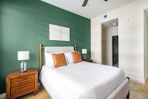 A hotel room with a bed, two bedside tables, a nightstand, a ceiling fan, and a door leading to another room. - Landing | Beautiful 1BD, Gym (College Station)