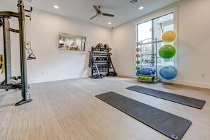 A spacious room with a ceiling fan, a gym area with exercise equipment, and a rack of colorful exercise balls. - Landing | Stunning 1BD, Game Room, Gym (Houston)