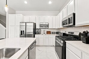 A modern kitchen with white cabinetry, stainless steel appliances, and a marble countertop. - Theater Area | Games Area | Private Pool (Davenport)