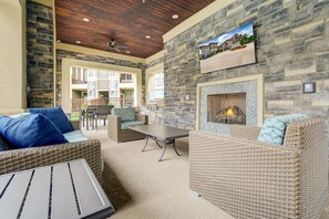 Un patio exterior con mobiliario de mimbre, una pared de piedra, una chimenea y un televisor montado en la pared.