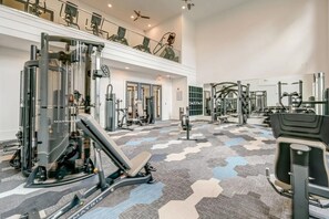 Un gimnasio amplio con diversas máquinas de ejercicio, piso estampado y un balcón con mobiliario.