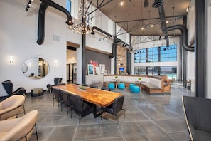 A spacious indoor area with a long wooden table, multiple seating options, and a view of the outdoors through large windows. - Landing | Chic 1BD, Gym, Clubhouse (Houston)