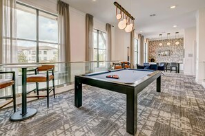 A pool table in a room with large windows, a dining area, and a patterned carpet. - Landing | Stylish 1BD, Gym, Game Room (Houston)