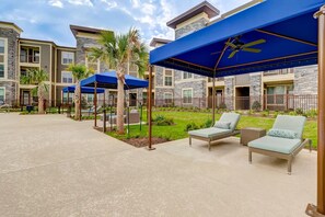A courtyard with outdoor seating, palm trees, and a stone building with multiple windows. - Landing | Stylish 1BD, Gym, Game Room (Houston)