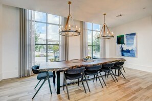 A spacious dining area with a long table, multiple chairs, and two pendant lights. - Landing | Stylish 1BD, Gym, Game Room (Houston)