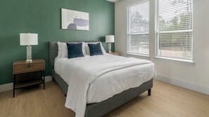 Ein Schlafzimmer mit einem Bett, zwei Nachttischen, einem Fenster mit Jalousien und einem Wandbild.