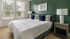 A bedroom with a bed, two bedside tables, a wall clock, and a window with blinds. - Landing | Modern 2BD in Deerbrook (Houston)
