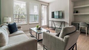A modern living room with a sofa, armchairs, a coffee table, and a TV mounted on the wall. - Landing | Modern 2BD in Deerbrook (Houston)