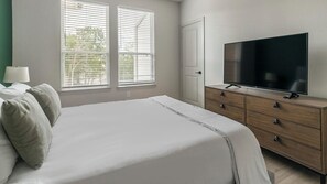A bedroom with a bed, a dresser, a television, and windows with blinds. - Landing | Beautiful 2BD in Deerbrook (Houston)
