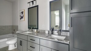 Een moderne badkamer met een wastafelmeubel met dubbele wastafel, een grote spiegel en een toilet.