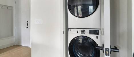 Una lavandería con dos lavadoras apiladas, una puerta y un interruptor de luz en la pared.