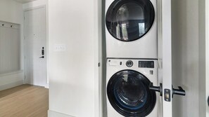 Una lavandería con dos lavadoras apiladas, una puerta y un interruptor de luz en la pared.