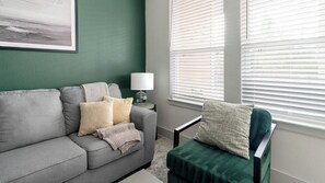 Ein Wohnzimmer mit einem grauen Sofa, einem grünen Sessel und einer Lampe auf einem Beistelltisch.