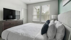 Quarto com cama, televisão, cómoda e janela com persianas.