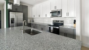 Een moderne keuken met roestvrijstalen apparatuur, een granieten aanrechtblad en witte kasten.