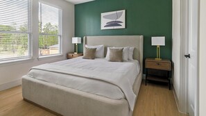 A bedroom with a bed, two bedside tables, a nightstand, a window with blinds, and a green wall. - Landing | Beautiful 2BD in Deerbrook (Houston)