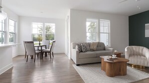 A modern living room with a sofa, coffee table, and dining area. - Landing | Modern 2BD, Game Room, Gym (Cape Coral)
