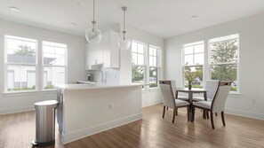 A modern kitchen with a central island, white cabinetry, and large windows providing natural light. - Landing | Modern 2BD, Game Room, Gym (Cape Coral)