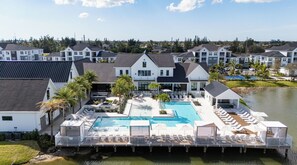 A resort with a large pool, lounge areas, and a dock extending into a body of water. - Landing | Modern 2BD, Game Room, Gym (Cape Coral)
