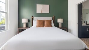 A hotel room with a large bed, two bedside tables with lamps, a painting on the wall, and a view of the outside. - Landing | Incredible 2BD, Gym, Game Room (Cape Coral)