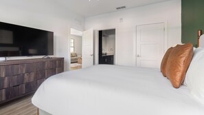 Ein Schlafzimmer mit einem großen Bett, einem Fernseher auf einer Holzkommode und einer Tür zu einem Badezimmer.