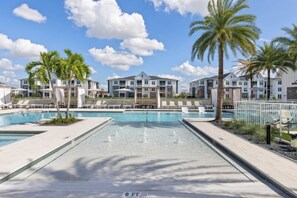 A swimming pool area with lounge chairs and palm trees, surrounded by multi-story buildings. - Landing | Incredible 2BD, Gym, Game Room (Cape Coral)