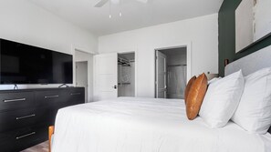 Ein modernes Schlafzimmer mit einem großen Bett, einem Flachbildfernseher, einer dunklen Kommode und einem begehbaren Kleiderschrank.