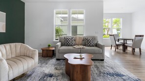 A modern living room with a sofa, armchair, coffee table, and dining area with chairs and a table. - Landing | Stylish 2BD, Gym, Game Room (Cape Coral)