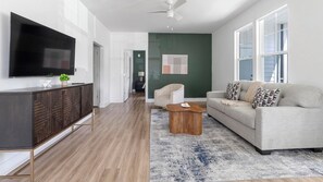 A modern living room with a flat-screen TV, a sofa, a coffee table, and a decorative rug. - Landing | Stylish 2BD, Gym, Game Room (Cape Coral)