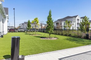 A residential area with a well-maintained lawn, a trash bin, and a black metal fence. - Landing | Stunning 2BD, Game Room, Gym (Cape Coral)
