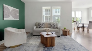 A modern living room with a sofa, a coffee table, and a chair. There are windows with a view of the outside. - Landing | Stunning 2BD, Game Room, Gym (Cape Coral)