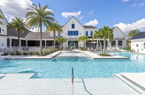 A swimming pool area with a building in the background, palm trees, and lounge chairs. - Landing | Modern 2BD, Gym, Game Room (Cape Coral)
