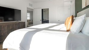 Ein Schlafzimmer mit einem großen Bett, einem Fernseher links und einer Tür zu einem Badezimmer.