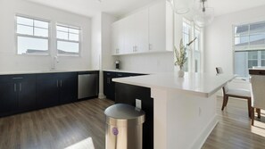 Una cocina moderna con una isla central, muebles oscuros y un cubo de basura de acero inoxidable.