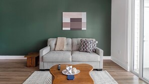 Una sala de estar con un sofá gris, una mesa de centro de madera y una obra de arte geométrica en la pared.