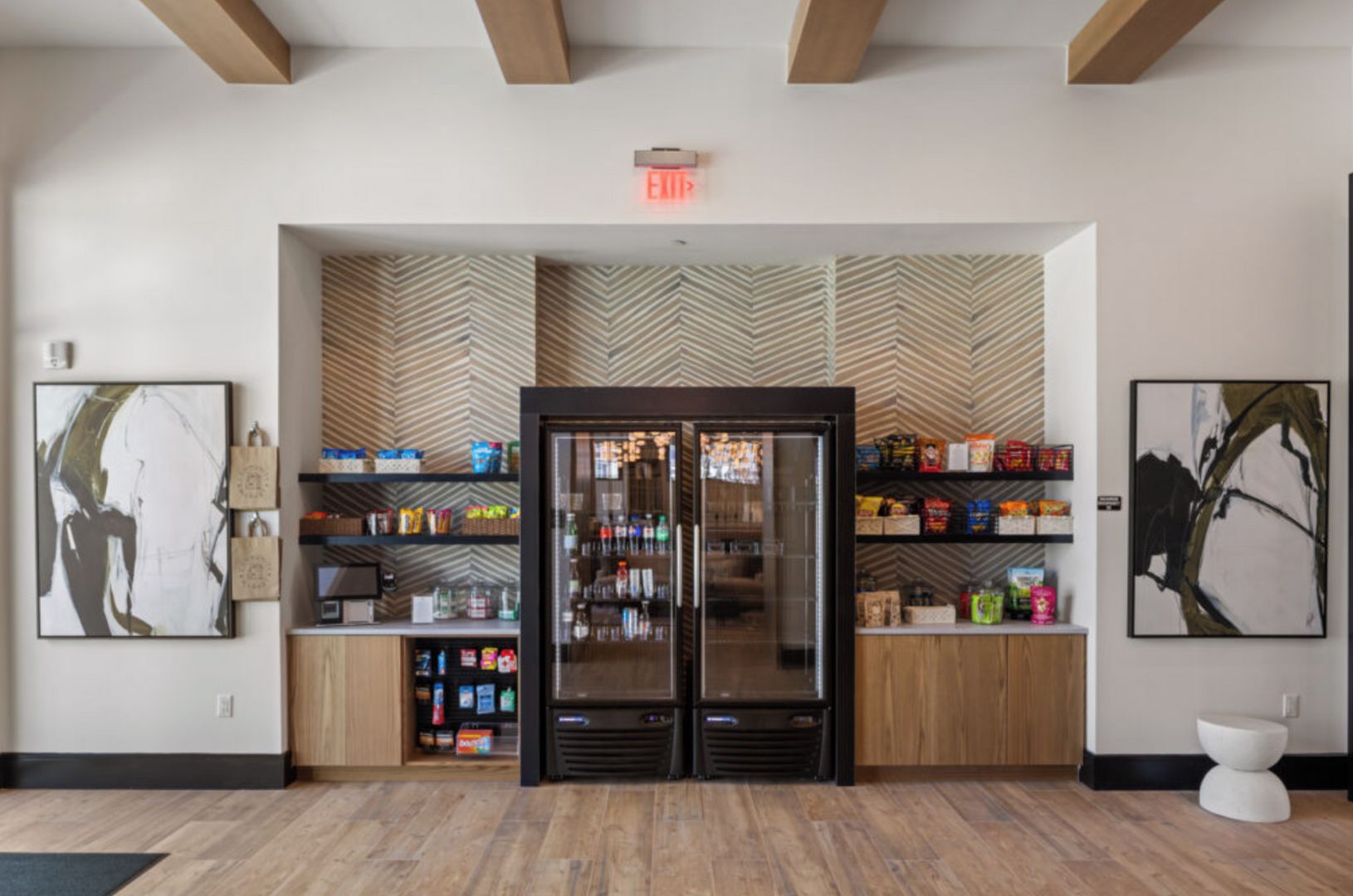 A modern lobby with a central glass door entrance, wooden flooring, and a herringbone-patterned wall.