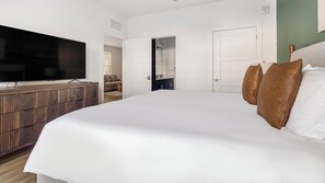 A modern bedroom with a large bed, a wooden dresser, and a television. - Landing | Stylish 2BD, Game Room, Gym (Cape Coral)