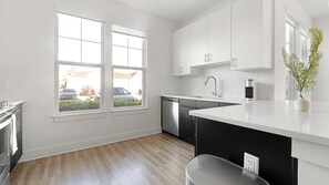 A modern kitchen with white cabinets, a dishwasher, and a sink. - Landing | Stylish 2BD, Game Room, Gym (Cape Coral)