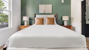 A bed with white bedding, two nightstands with lamps, a wooden headboard, and a green wall with a painting. - Landing | Stylish 2BD, Game Room, Gym (Cape Coral)