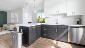 A modern kitchen with dark cabinetry, a stainless steel dishwasher, and a white countertop. - Landing | Incredible 2BD, Game Room, Gym (Cape Coral)